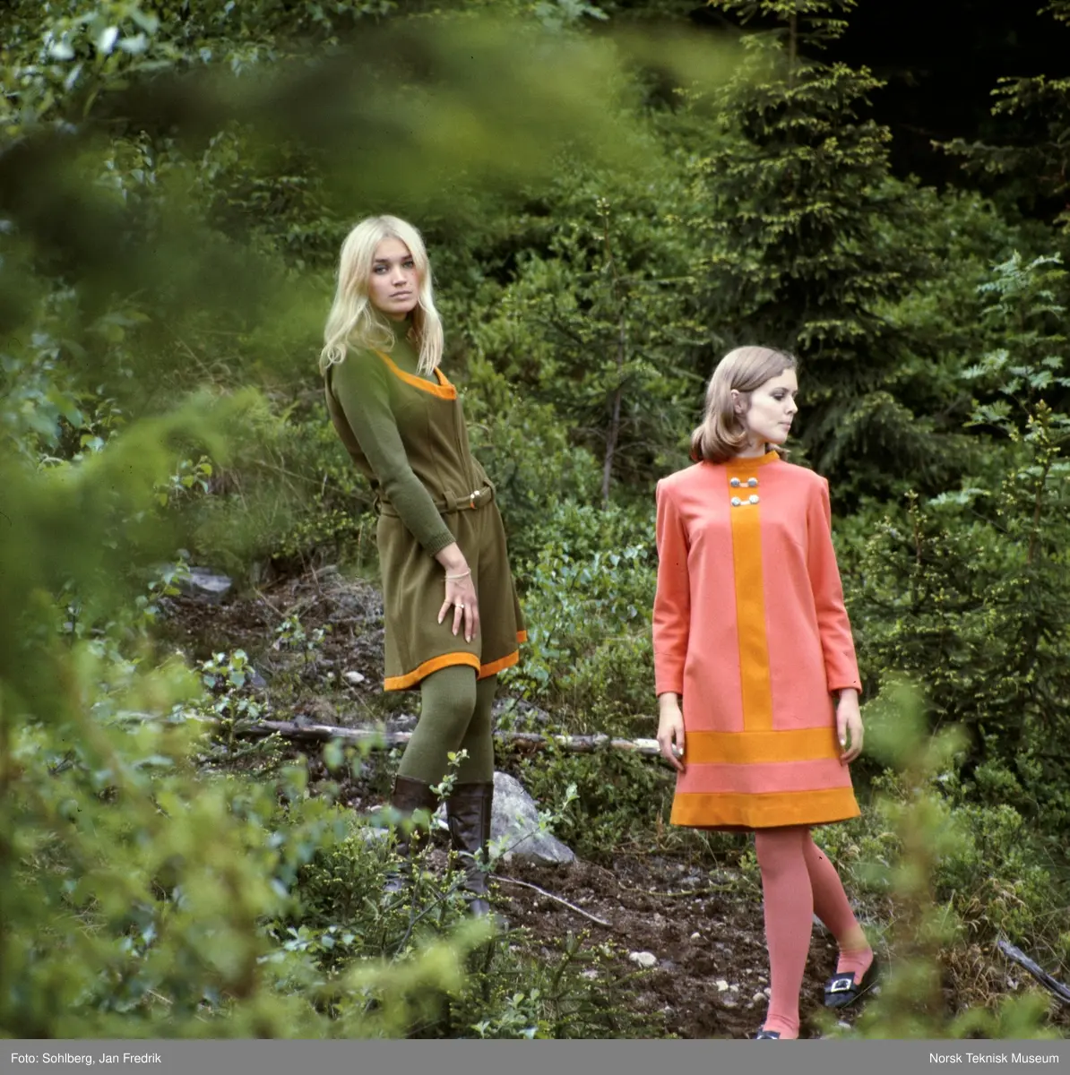 Motebilde, to kvinner poserer i skogen i klær fra kolleksjonen "Fjord Look", høsten 1968. Bildet er en del av en serie der noen er publisert i ukebladet Det Nye. Billedtekst: I forgrunnen ser du Joan i en ørretfarget kjole med høstfarget innfelling, både i stripe ned foran og som to striper nedentil. Stoffet er 90% ull og 10% nylonforsterkning. Prisen er ca kr. 156,-. Den morsomme ermeløse buksekjolen i "mose" med belte og høstfargede kantinger er vel midt i blinken denne sesongen. Stoffet er ull/ nylon og prisen er ca kr. 154,-."