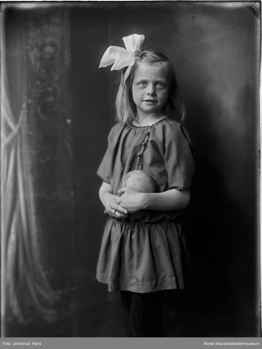 Portrett av jente stående i studio med ball i hendene og sløyfe i håret.