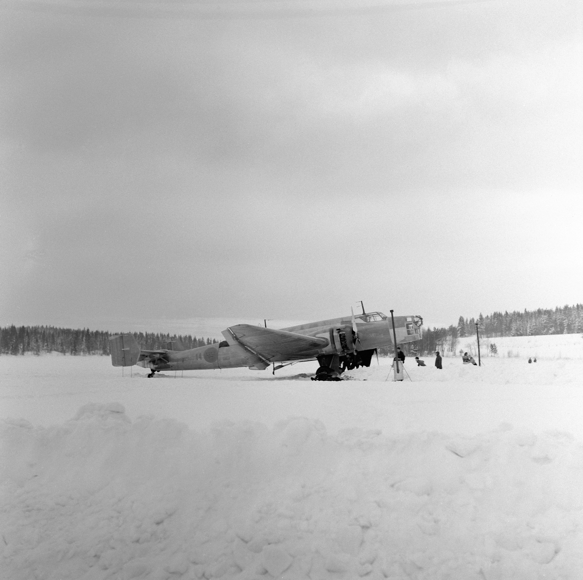 Flygplan B 3 nödlandad på Storsjöns is efter flygning i hårt väder i februari 1946. Flygvapenpersonal vid flygplanet. Vy från sidan.