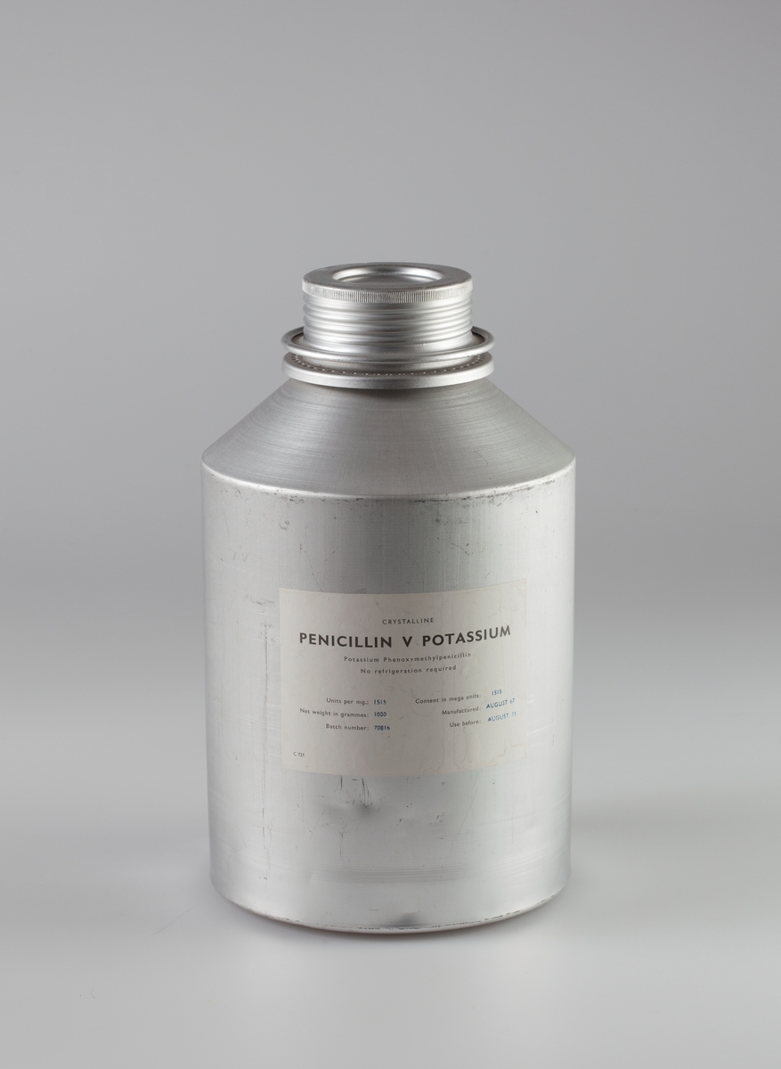 Sylinderformet aluminiumsbeholder med skrulokk. Påklistret papiretikett med navn på innhold.