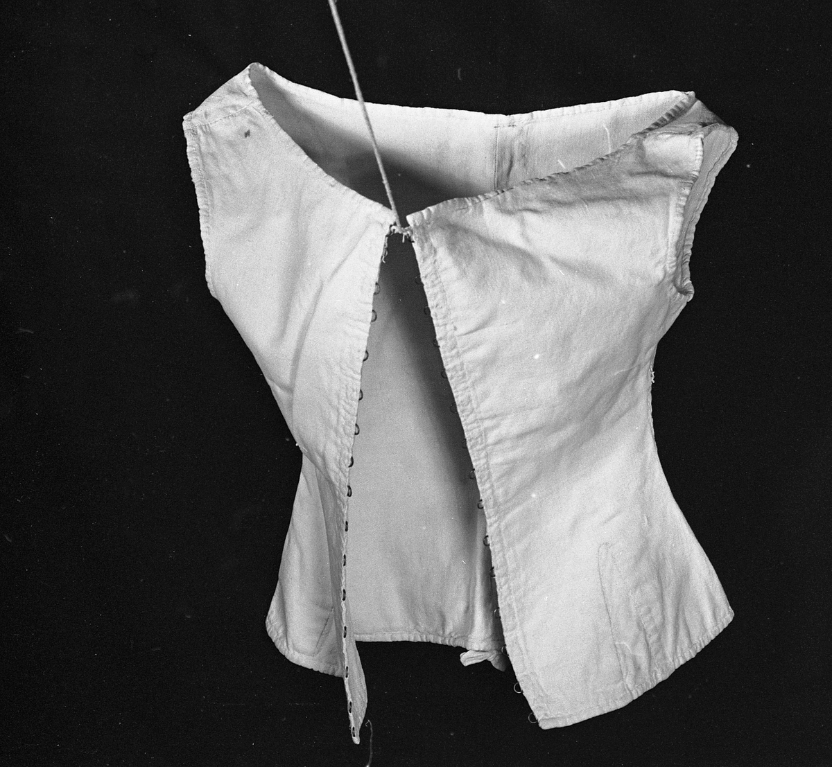 Liv eller korsett av lin med metallhekter og tvunnet tråd til snøring. Det har søm midt bak med hempe oppe og nede. Sidesømmen er litt tilbaketrukket, og det er felt inn stoff neders i sida for utsving fra livet. Halsåpningen er båtformet.