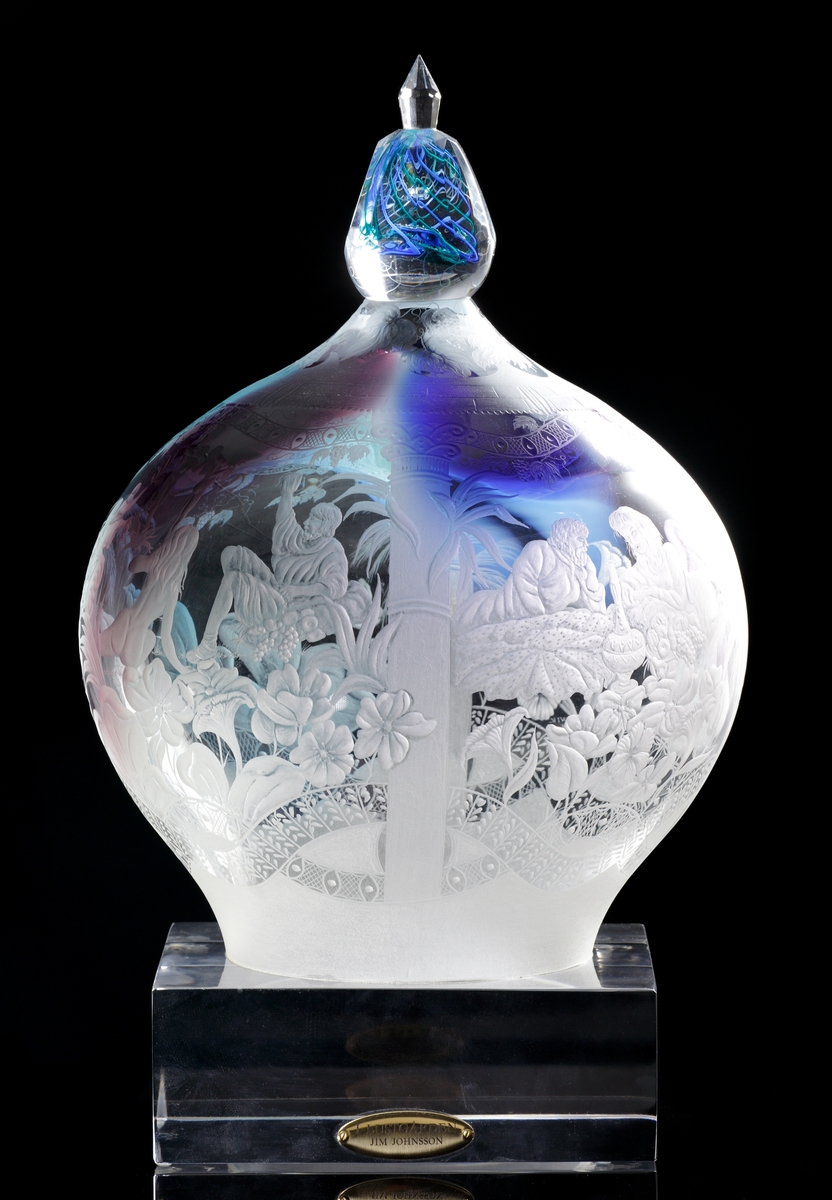Fyrkantig glassockel. Droppformad skulptur som avslutas med en slipad knopp. I knoppen gröna och blå linjer. Skulpturen graverad med detaljerat motiv från Edens lustgård.