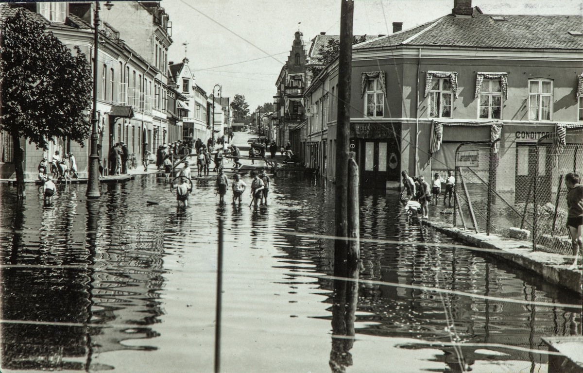 Postkort, Hamar, Strandgata, flommen i 1927. Mjøsflommen 1927, Barn leker i flomvannet i Strandgata, Enggata utenfor Victoria hotel, baker Johannessen,