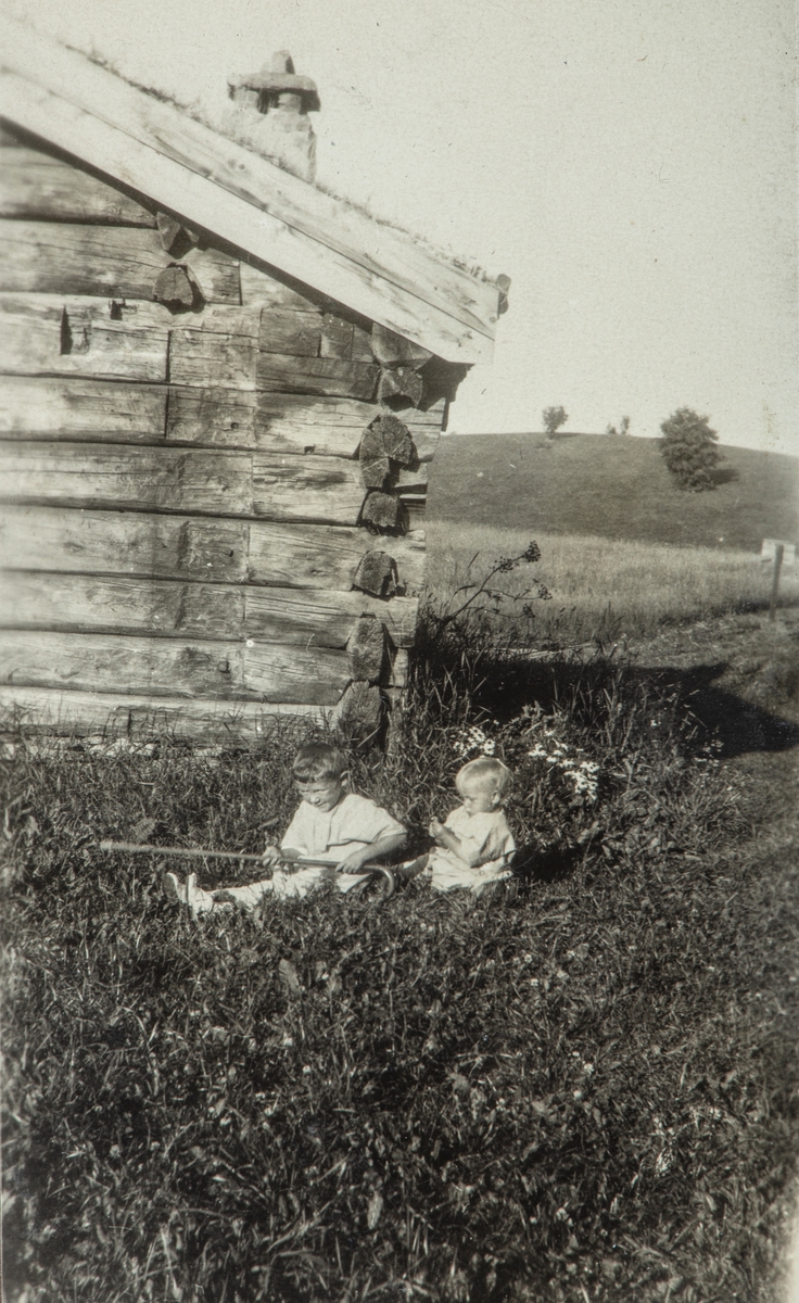 2 barn sittende i gresset utenfor et av husene på Domkirkeodden sommeren 1923. Fra venstre Hans Jørstad og Yngve Jørstad.