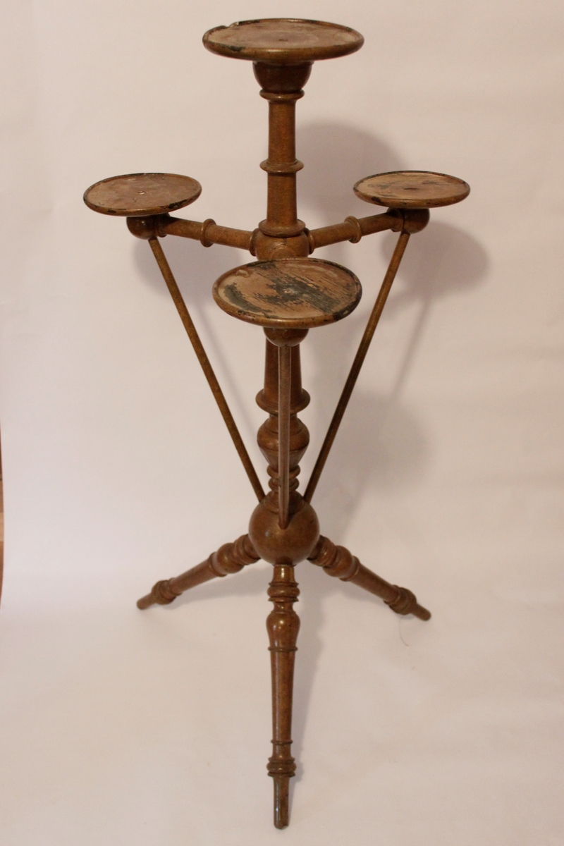 Piedestal med plats för fyra krukor. En högst upp i mitten och tre en bit ner runt den mittersta. Piedestalen har formen av en pelare som delar sig i tre snedställda svarvade ben nedtill.