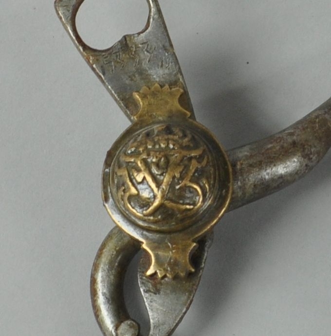 Bissel med kjegleformet stang, leddet på midten. Krumme sidestenger med hull for tøyler. Runde knapper på sidene av messing, med dekorativt motiv av monogrammet til Fredrik V.