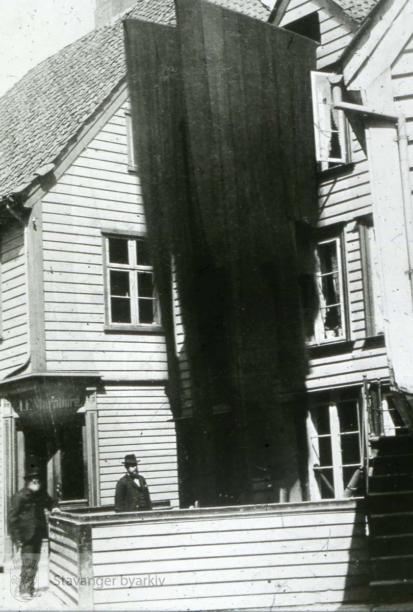 Østervågs sørligste hus fra sør...Fra venstre Østervåg 7, Østervåg 5 og Østervåg 3. Eiendommene tilhørte i 1899 kjøpmann I. F. Marnburg, farger Ole Hansen og til høyre det såkalte Dalva-huset som ble revet like etter. Bildet er tatt i forbindelse med reguleringsplaner for strøket. Farger Hansen står i hagen sin, som er tørkeplass.