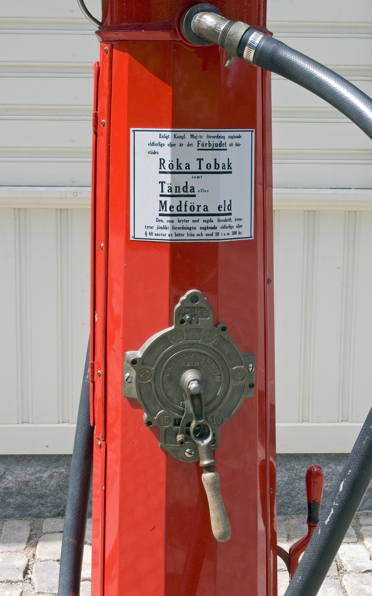Bensinpump, fabriksgjord. Överst sitter en glasglob, SKAFOR.0015125 på ett metallfäste.  Under globen en cylinder av glas med mätmekanism och gradering. Därunder kommer det rödlackade pumphuset av stål. På en sida sitter en etikett av metall med text: Enligt Kungl. Maj:ts förordning angående eldfarliga oljor är det Förbjudet [understruket] att härstädes Röka Tobak [understruket] samt Tända [understruket] eller Medföra Eld [understruket]. Den som bryter mot sagda föreskrift, äventyrar jämlikt förordningen angående eldfarliga oljor § 60 ansvar av böter från och med 10 t.o.m. 500 kr." Etiketten sitter strax ovanför ett pumphandtag med omgivande dekorativt utformade "bricka" av metall och handtag svarvat av trä. "Brickan" är rund och utformad med graderingar från 0 till 25 med femliters intervaller. Text: PUMP IV-SC 54 A.B. J.C. LJUNGMAN MALMÖ VICI No 6705, ett räkneverk och LITER. Till höger om detta sitter ett annat pumphandtag av rödlackerat stål, fäst nertill. Ovanför etiketten börjar bensinslangen av gummi i ett metallfäste. Den fortsätter i en böj neråt till vänster, runt och upp och avslutas av den utgående kranen av metall, som hänger i ett hål på cylindern. Där bredvid finns också en låsbar lucka.