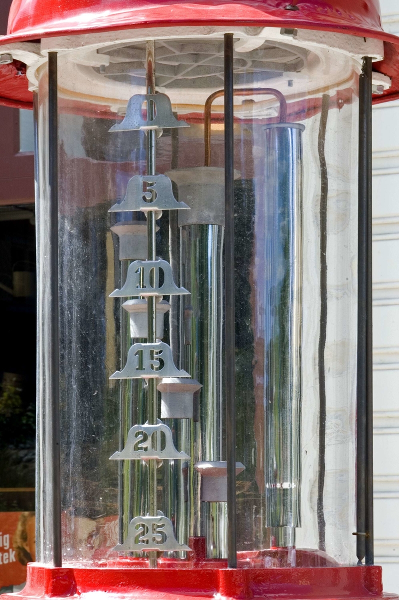 Bensinpump, fabriksgjord. Överst sitter en glasglob, SKAFOR.0015125 på ett metallfäste.  Under globen en cylinder av glas med mätmekanism och gradering. Därunder kommer det rödlackade pumphuset av stål. På en sida sitter en etikett av metall med text: Enligt Kungl. Maj:ts förordning angående eldfarliga oljor är det Förbjudet [understruket] att härstädes Röka Tobak [understruket] samt Tända [understruket] eller Medföra Eld [understruket]. Den som bryter mot sagda föreskrift, äventyrar jämlikt förordningen angående eldfarliga oljor § 60 ansvar av böter från och med 10 t.o.m. 500 kr." Etiketten sitter strax ovanför ett pumphandtag med omgivande dekorativt utformade "bricka" av metall och handtag svarvat av trä. "Brickan" är rund och utformad med graderingar från 0 till 25 med femliters intervaller. Text: PUMP IV-SC 54 A.B. J.C. LJUNGMAN MALMÖ VICI No 6705, ett räkneverk och LITER. Till höger om detta sitter ett annat pumphandtag av rödlackerat stål, fäst nertill. Ovanför etiketten börjar bensinslangen av gummi i ett metallfäste. Den fortsätter i en böj neråt till vänster, runt och upp och avslutas av den utgående kranen av metall, som hänger i ett hål på cylindern. Där bredvid finns också en låsbar lucka.