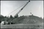 Badelunda sn, Anundshögsområdet, Långby.
Kranbil lyfter upp något på toppen av Anundshögen.