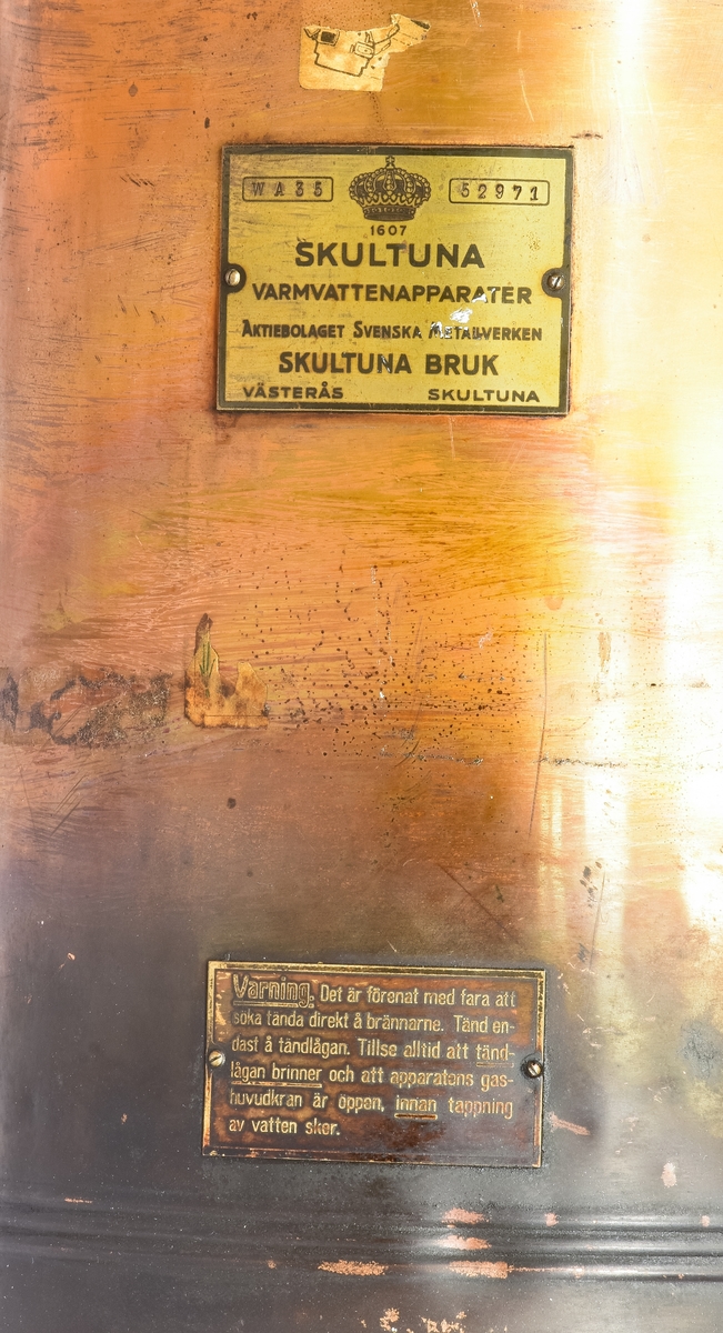 Bronsfärgad varmvattenberedare med texten "Skultuna Varmvattenapparater aktiebolaget Svenska metallverken Skultuna bruk Västerås Skultuna" , WA 35, 52971 på sig.