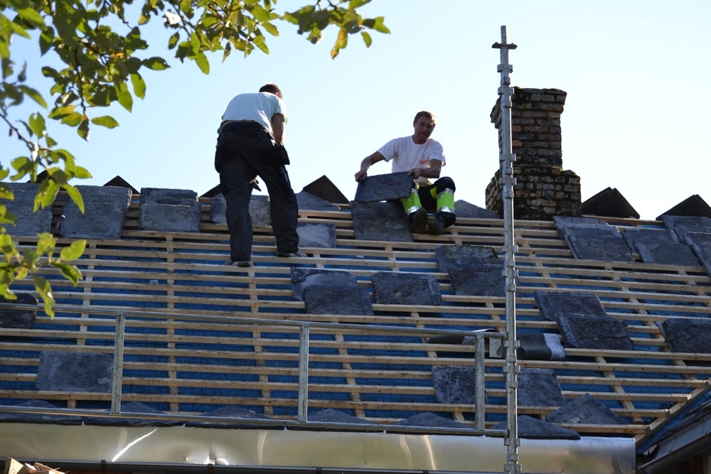 Leirfjord, Nedre-Leland. Entreprenørfirmaet, Einmo, legger om taket på Bergh-brygga (museet). Snekkere hos Einmo bærer stein på plass på taket etter opplektingen.