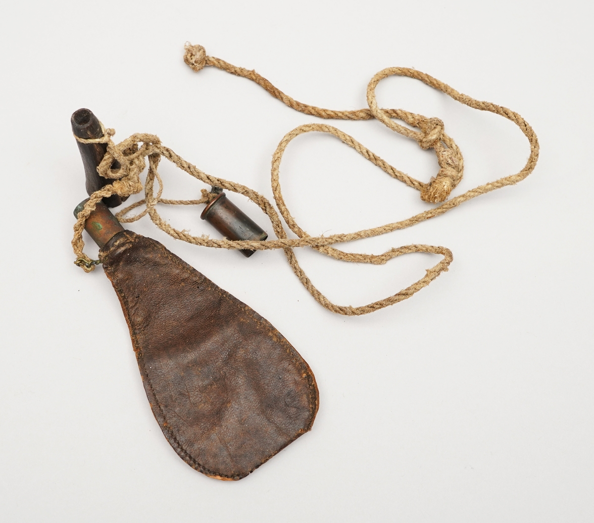 Krutpung. Brun skinnpose med opning der det er sett inn ein sylinder i metall. Sydd med jamne sting på langsidene. Snor fest i enda, med to objekt fest på, ein metallsylinder med botn, ein gjenstnad truleg av horn (eller bein) med trebotn.