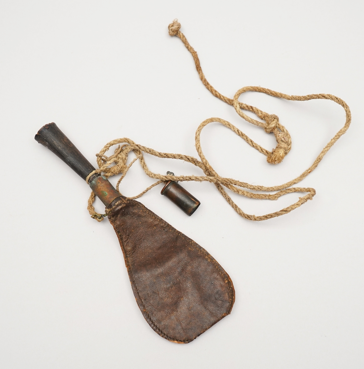 Krutpung. Brun skinnpose med opning der det er sett inn ein sylinder i metall. Sydd med jamne sting på langsidene. Snor fest i enda, med to objekt fest på, ein metallsylinder med botn, ein gjenstnad truleg av horn (eller bein) med trebotn.