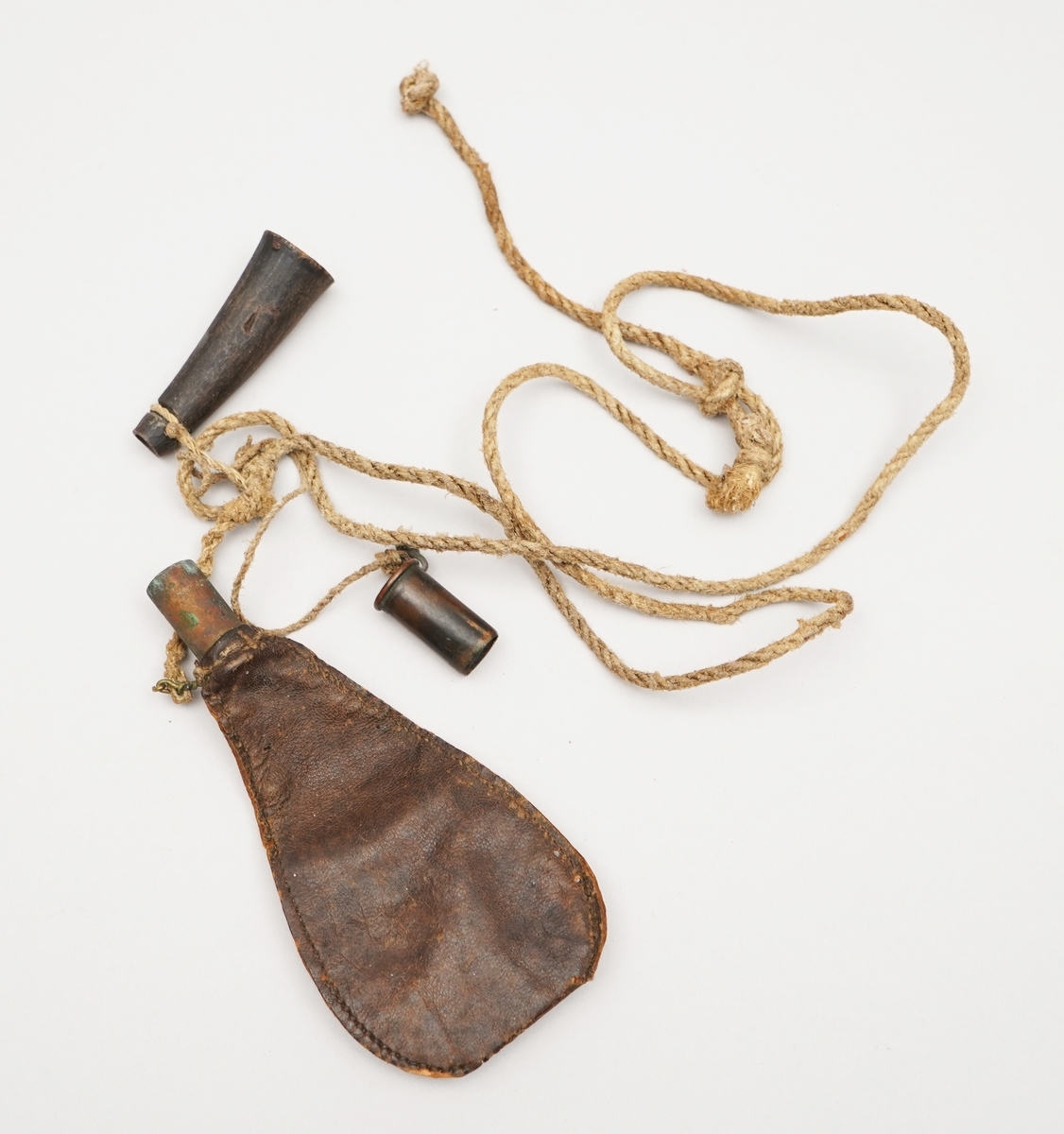 Krutpung. Brun skinnpose med opning der det er sett inn ein sylinder i metall. Sydd med jamne sting på langsidene. Snor fest i enda, med to objekt fest på, ein metallsylinder med botn, ein gjenstnad truleg av horn (eller bein) med trebotn.