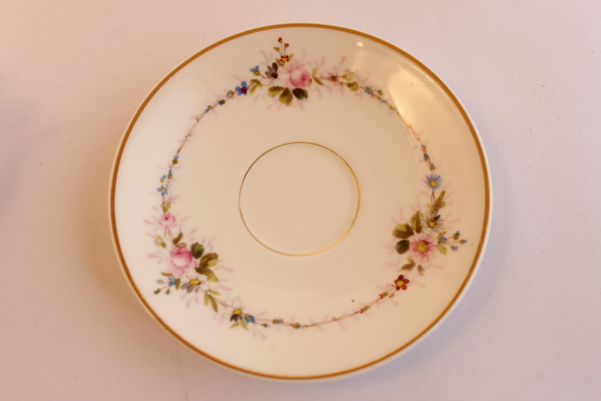 Handmålade mycket tunna porslinskoppar för kaffe. Kopp och fat är båda vita med guldkant. De är dekorerade med ett blommönster som är målat för hand.  Bland annat en ros samt en girland som sträcker sig runt både kopp och fat. Motivet med blommorna upprepas tre gånger runt både kopp och fat. 
Koppar och fat är handmålade av en släkting till givaren under senare delen av 1800-talet.