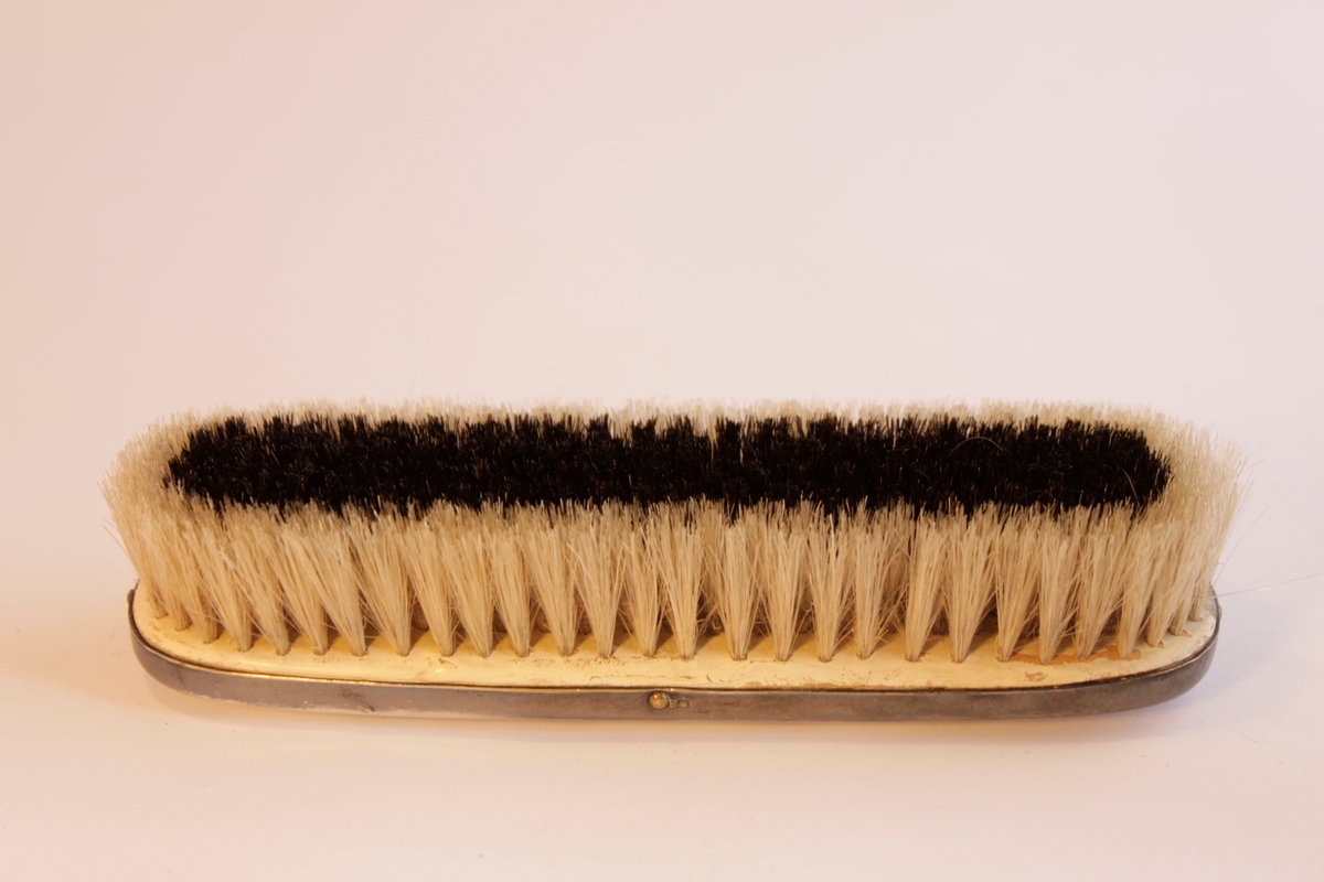 Borstgarnityr bestående av tre borstar en (a) hårborste, två klädesborstar (b-c). Naturborst. Borstarna är klädda i nysilver som har ingraverade stiliserade blommönster. Hårborsten och den ena klädborsten har namnet "Axel" ingraverat på ovansidan. Själva borsthuvudena är tillverkade av trä och sedan har en plåt av nysilver spikats på.