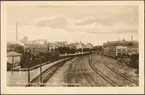 Vy på bangård och stad med fabriker i bild.