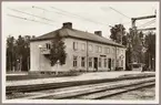 Stationshus och perrong vid elektrifierad bangård.