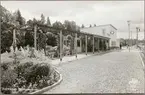 Vy på stationshus och kiosk med resande vid kiosk.