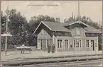 Spårsida av station med vy på stationshus och perrong med personal.