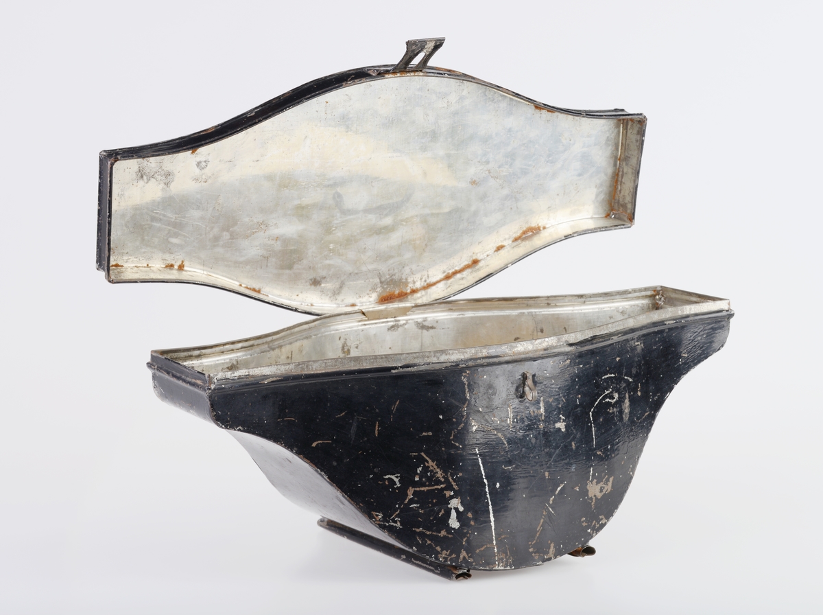 En hatteboks (FTT.56303.01) som inneholder en snutehatt (FTT.56303.02), et bandolær (FTT.56303.03) og en epålett (FTT.56303.04).  
FTT.56303.01:
Hatteboksen er laget av blikk og er svartlakkert utenpå. Lokket er hengslet på baksiden. Oppå lokket er det et enkelt håndtak. I fronetn er det en hempe for hengelås. Den har to lave bein som er laget av sammenrullet blikk. Boksen har form tilpasset hatten. Esken har ikke fôr, men det ligger et papir i bunnen.
FTT.56303.02:
En svart uniformshatt, nærmere bestemt en snutehatt eller en tosnutet hatt. Det er gullbånddekor på hver snute. På den ene siden er det festet en stor kokarde i rødt, hvitt og blått. Over denne er det to flate gullbånd som ender i en spiss. I enden er det en gullfarget metallknapp med et anker med en kongekrone over. Hatten er laget av svart silkefloss med svarte silkebånd langs kanten. Hatten har hvitt silkefôr og svettebånd av brunt lær. På svettebåndet er det festet brune skinnreimer til å feste under haken. På den ene siden er det festet en hvit silkesløyfe. Silkefôret har informasjon om produsent, se "Påført tekst/merker". Det er også bilde av en edderkoppe og et edderkoppnett. Hatten har avstivning ved hjelp av papp. Hatten er håndsydd.
FTT.56303.03:
Et bandolær laget av svart skinn, svart silkestoff og messing. Midjebeltet har en spenne midt foran. Spennen har motiv av et anker med en krone over. På innsiden av beltet er det sydd fast en skinnreim med metallhull til å regulere livvidden. Skulderreimen er festet i midjebeltet med metallringer. Delene til skulderreimen festes sammen med to fjærbelastende kroker. Ved sammenføyningen skulderreim og midjebelte er det påmontert en liten kjetting med krok.
FTT.56303.04:
En skulderklaff til uniform. Oversiden består av svarte- og gullfargede flettede snorer. På undersiden er det sydd på svart ullstoff som er like bred som klaffen. I den ene enden er det sydd på en svart knapp som ullstoffet kan festes i.