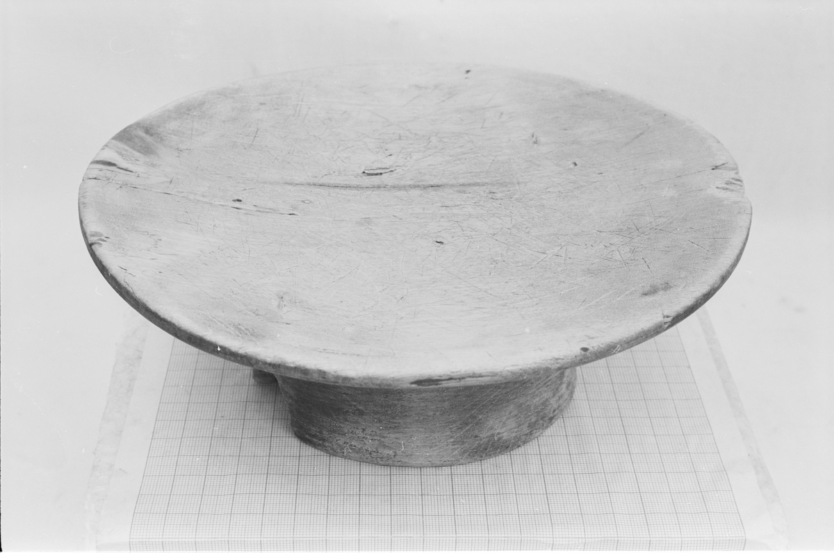 Rundt fat på stett med en svak fordjupning. På undersida er det skåret et mønster (en enkel geometrisk bord)