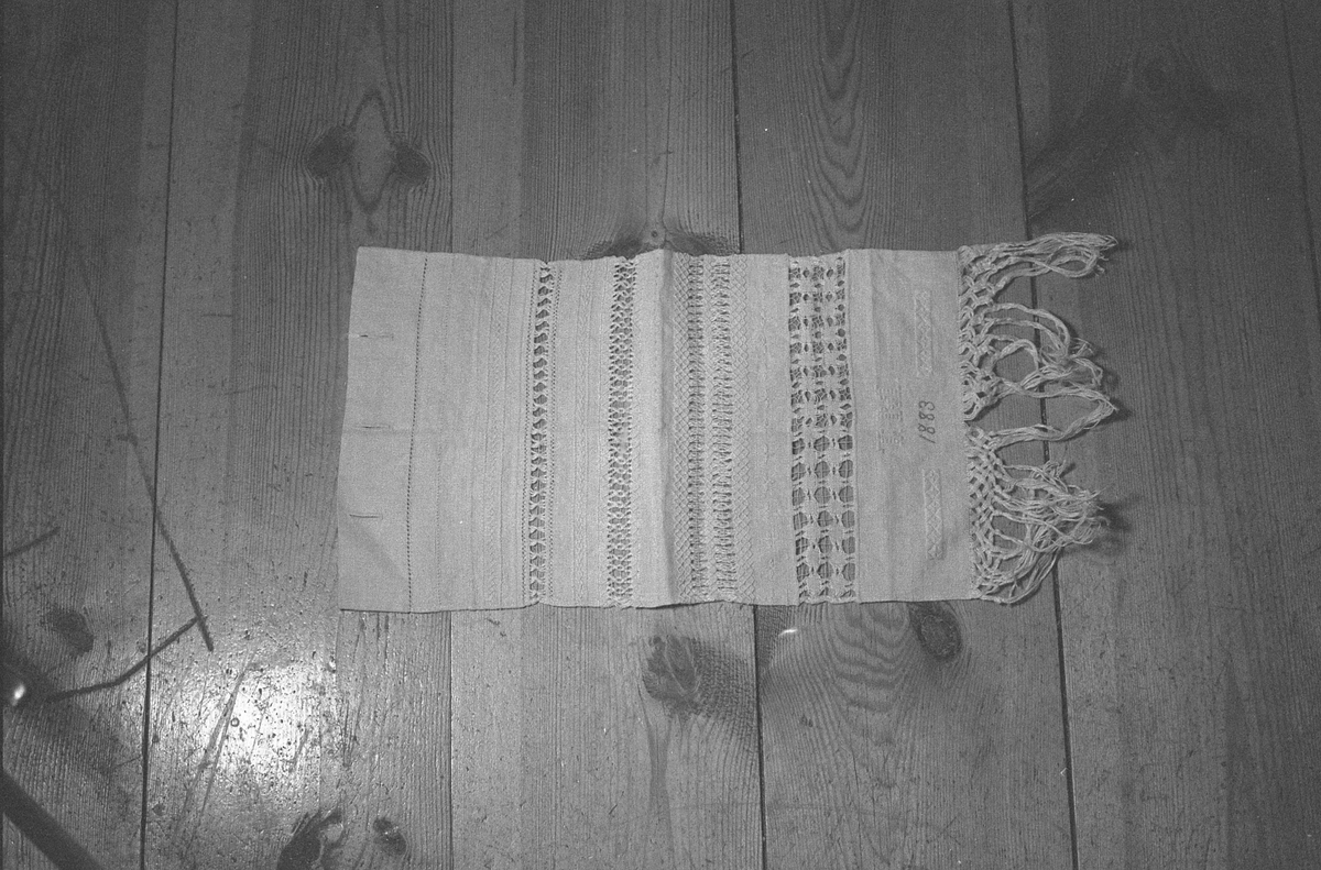 Avlangt lerretsvevd stoff med frynser nede og ulike sømteknikker, herunder broderi og uttrekkssøm