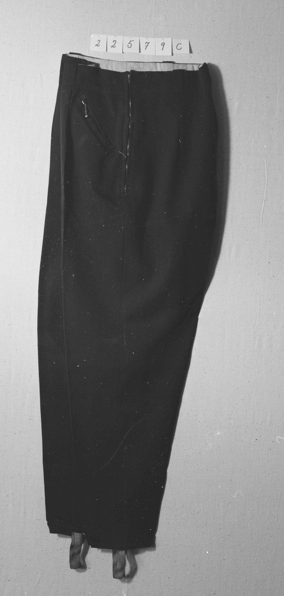 Overdel til drakt bestående av et kypertvevd blått bomullstoff brodert med ullgarn og med ermer og krage av lerretsvevd ull. Front og ermer har tinnknapper med støpt mønster. Det er hekter og trykknapper til å lukke med.
Buksa til drakta er av typen strekkbukse med press og strikk under beina. Den har glidelåslukning i siden og to lommer med glidelås i front.