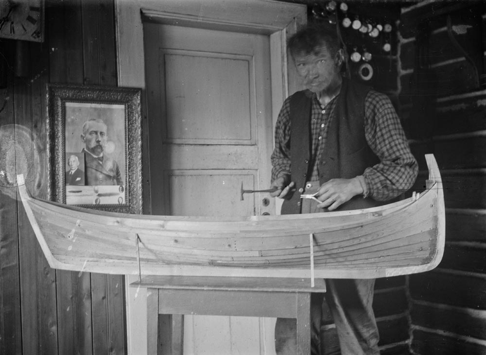 Leirfjord, Ulvangen, Myrvang. Kornelius Myrvang arbeider med modellen av en Nordlandsfembøring i stua på Myrvang. På veggen henger et bilde av Fridtjof Nansen og mange klokker.