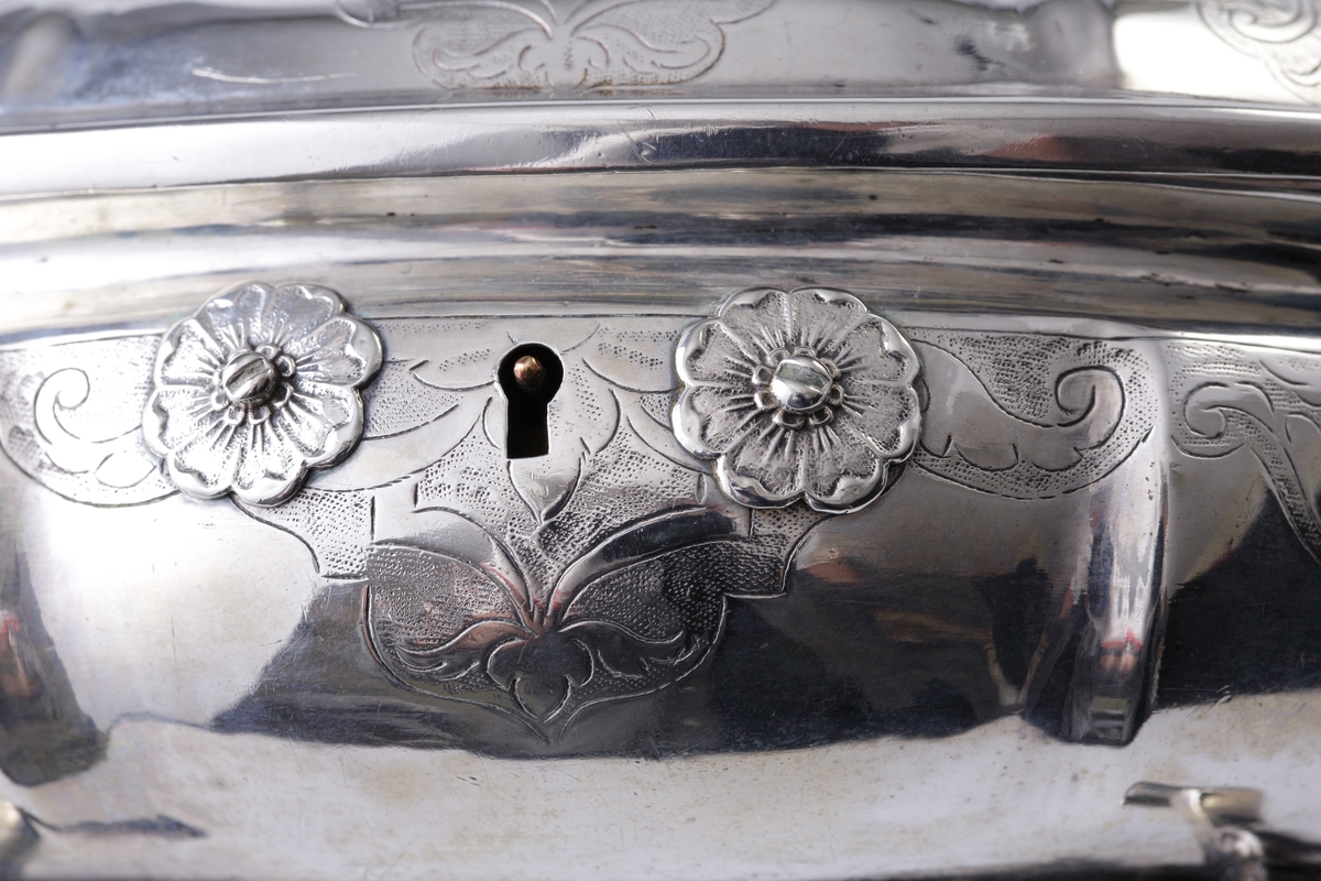 Sockerskrin i silver.
Oval modell. Graverade lambrekäng(?)bårder längs det bukiga livet. Nyckelhålet omges av två blommor i relief (nyckel saknas). Står på fyra inåtvända fötter. På locket ett ornerat spegelmonogram: "AG" (?).  
Stämplar (ofullständiga) + åldermansranka på undersidan av skrinet.