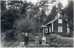 Himmeta sn, Struthagen.
Porträtt utanför huset: Lars och Anna Andersson, fosterdottern Veddla.