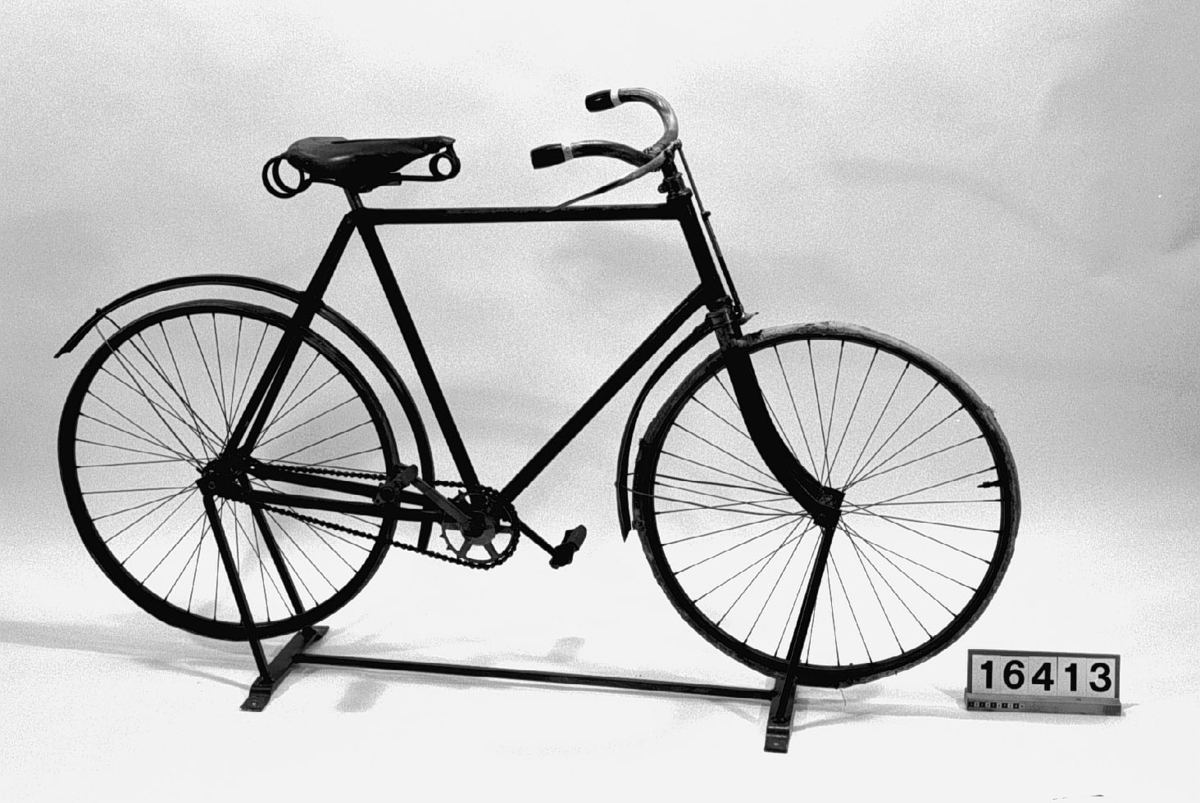 Tvåhjulig cykel med luftringar och fast kedjedrift på bakhjulet. Ram av stålrör med skärmar av plåt och fjädersadel klädd i läder. Ringklocka på styret. Svart med gröna ränder på skärm. Höger pedalvev och kedjekrans utbytta liksom skärmar och fälgar.