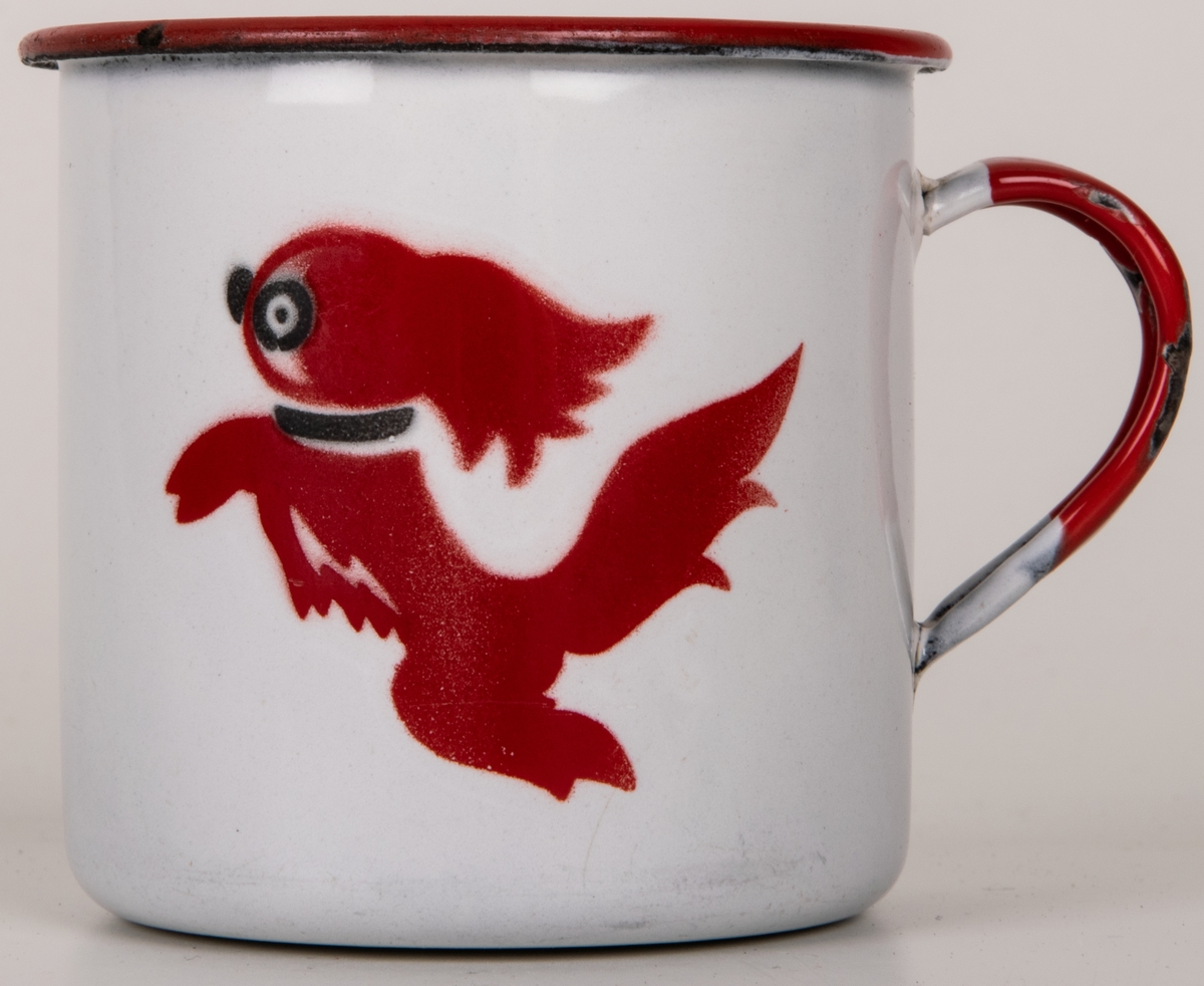 Mugg i vit emaljerad plåt. Cylindrisk med omvikt mynningskant. Lodgrepe. Kant och grepe röda. Dekor i rött och svart: hund (formgiven av Einar Nerman). Blå stämpel under: KOCKUMS (logotyp med texten K.E.R. SWEDEN) 7 cm NERMAN.