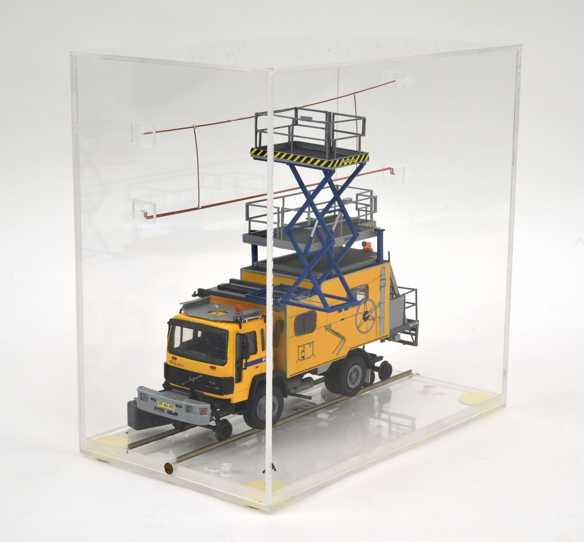 Modell i skala 1:50 av elrevisionsbil typ VRB från SRS Swedish Rail System AB baserad på ett lastbilschassi av typ Volvo FL6 för Nederlandse Spoorwegen (NS). Fordonet är gulmålat med blå detaljer i enlighet med NS:s färgsättning och på förarhyttens sidor bakom dörrarna finns NS logotyp. Flakdelen utgörs av ett skåp med fönster på sidorna samt ingång från bakre gaveln. Skåpet är gult med avbildningar av kontaktledningar. Längst bak och på skåpets tak finns fasta arbetsplattformar med skyddsräcken. På främre delan av skåpets tak finns en saxlyft med blå ben i uppfällt läge. Bilen har utöver de vanliga lastbilshjulen en enaxlad rälsboggi fram och en tvåaxlad boggi bak och modellen visar bilen i rälskörningsläge. Den främre kofångaren är framdragen och fungerar som fäste för boggien. Modellen har holländska registreringsskyltar.

Modellen är monterad i en plexiglasmonter och står på en räls av metall som är lagd direkt på monterns golv utan slipers. Ovanför bilen finns en kontakledning av koppar fäst i monterns väggar. Lastbilens bränsletank har lossnat och ligger lös i montern.
