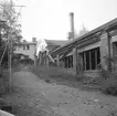 Hjulsbro ABs fabrik inför rivning. Här dokumenterad av Östergötlands museum 1977. Verksamheten på platsen startade 1907 genom grundandet av Hjulsbro Tråddrageri- och Spikfabrik. Från 1923 ägdes fabriken av den kände bankdirektören Jonn O. Nilsson i Linköping och med honom kom verksamheten åter på fötter efter en svår period under  krigsåren och följande depression. Fabriksbyggnaden på bilden uppfördes på platsen för en äldre som blivit lågornas rov 1930. Från 1964 ägdes företaget av Halmstad Järnverk, i folkmun Hamstadstål. I bakgrunden skymtar fabrikskontoret med arbetarebostäder.