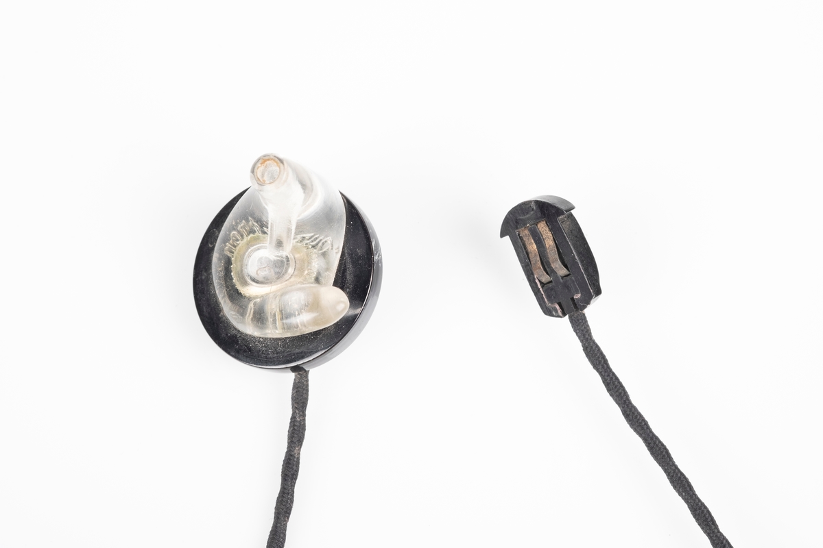 Ørepropper som kobles til radioen. Den har svart flettet ledning og propp i plast som kan fjernes fra ledningen. Den ene proppen mangler.