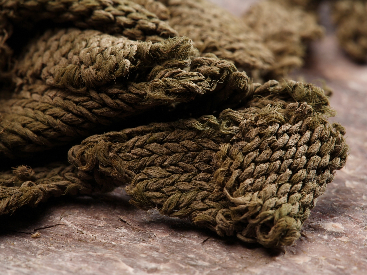 Flertalet mindre grågröna stickade fragment eventuellt av siden, stickade i slätstickning. Tråd samt mask och varvtäthet: 2-trådigt Z-spunnet, S-tvinnat masktäthet: 4-6 maskor/cm varvtäthet: 5-7 varv/cm.