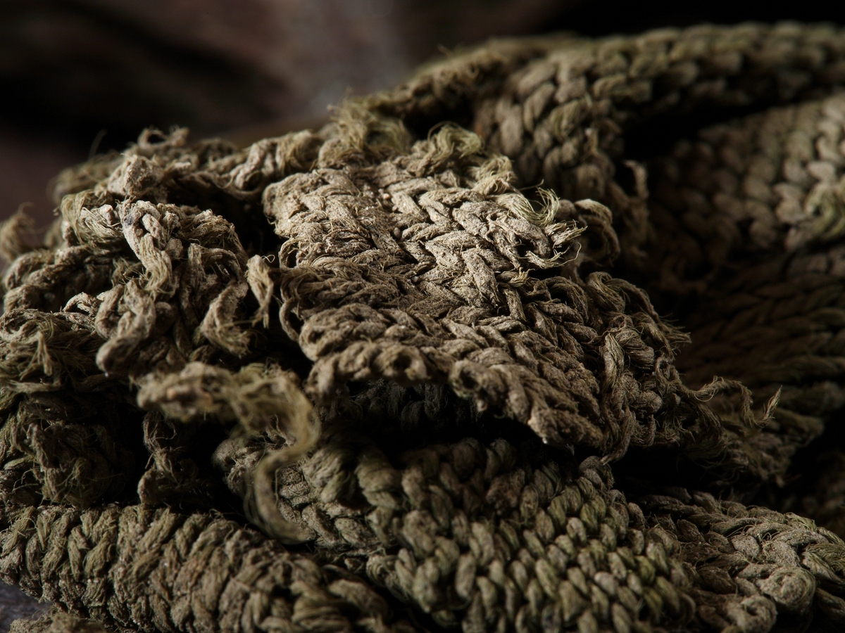 Flertalet mindre grågröna stickade fragment eventuellt av siden, stickade i slätstickning. Tråd samt mask och varvtäthet: 2-trådigt Z-spunnet, S-tvinnat masktäthet: 4-6 maskor/cm varvtäthet: 5-7 varv/cm.