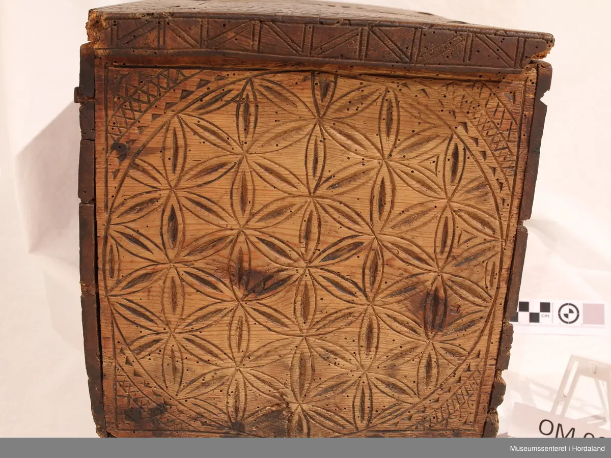 Mellomstor trekvit kiste i furu, rikt dekorert med skoren ornamentikk midt på loket, på bak- og frontsida, ellers rikeleg rosettornamentikk. Utskjeringane skal syne dei 4 årstidene. Skrinet luktar kamfer. Naglane fungerer som ei slags sikring. Skrinet har to jernhengsler og beslag på innsida av loket.