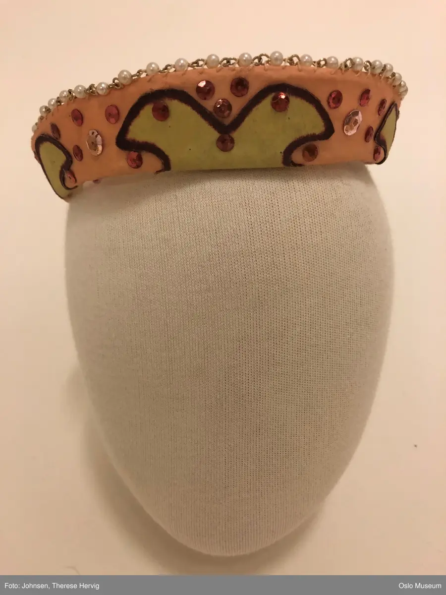 Todelt ballettkjole som holdes sammen med knapper.
A Innsvingt liv, holdes sammen med hekter i ryggen. Tynne skulderstropper i strikk. Blek rosa/ ferskenfarget bunn med innfellinger i mørkere rosa. Utringing er dekorert med grønn kant. 
B: Strutteskjørt i blek rosa, fersken med innfellinger i mørkere rosa. Dekorert med applikerte blomster i rosa, gul og brun. Mørk rosa bånd i livet som knytes i sløyfe på ryggen. Skjørtet lukkes med hekter og knapper i rygg. 
C: hodepynt, avstivet, kledd i samme tekstil som resten av kostymet. Dekorert med rosa paljetter. 
D: ferskenfarget erme med innfellinger i mørkere rosa. 
E: ferskenfarget erme med innfellinger i mørkere rosa.