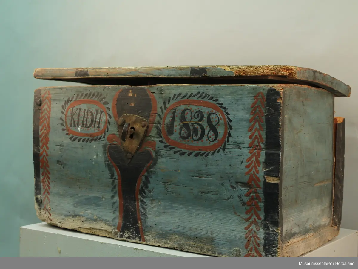 Blå rosemåla trekiste. Loket er hengsla. "KHDH 1838" er måla på framsida. Lås med nøkkel på framsida. Kista er i dårlig stand.