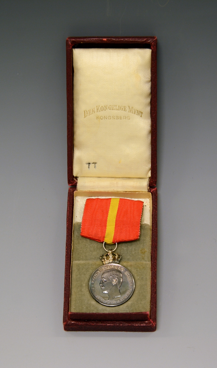 Medaljen ligger i en liten, flat, burgunderrød eske (original-etui) - preget med en forgylt krone på lokket. Silke og fløyel innvendig.