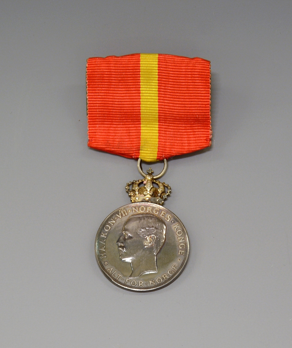 Medaljen ligger i en liten, flat, burgunderrød eske (original-etui) - preget med en forgylt krone på lokket. Silke og fløyel innvendig.