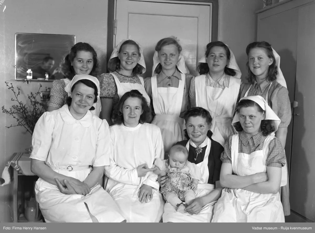 Sanitetsforeningens Fødehjem, Vadsø. Bildet viser en del av personalet og en baby.. Jordmor Elisabeth Pedersen nr 2 fra venstre i første rekke og Elisabeth Methi nr 3 fra venstre i andre rekke. I Vadsø bygde sanitetsforeningen et stort fødehjem med legekontor og kontrollstasjon for mor og barn. Fødehjemmet er bygd i 1952, arkitekt Finn Eidvin og hovedentreprenør Alrik Basma.  Fødehjemmet ble lagt ned i 1966.
Kilde: "Trond M.E.Dancke "Opp av ruinene, Gjenreisning av Finnmark 1945-1960."
