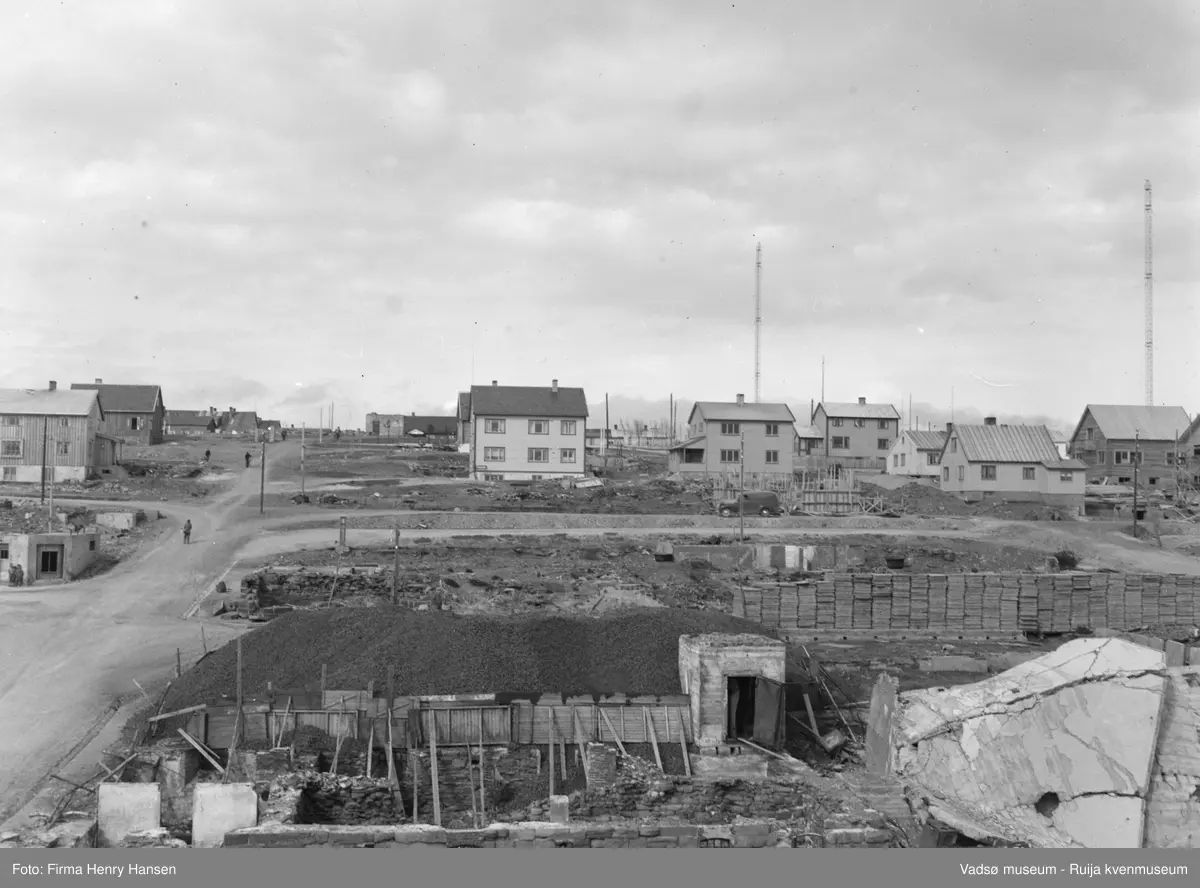 Vadsø Sentrum 1948. Bildet er tatt fra Vadsø torg mot nord. I forkant av bildet ruiner, rester av grunnmur og et kullager. Til venstre i bildet Tollbugata som krysser Havnegata og Nyborgveien opp mot Damsveien. Vi ser skomaker Sarajervis hus i Nyborgveien. Midt i bildet; Langs Oscarsgate og Inspektør Hansensgate flere gjenreisningshus.  Basmagården i Oscarsgate 3 er under oppføring. Radiomastene ses i bakkant av bildet.