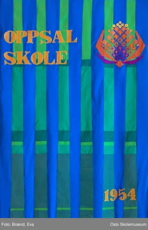 En stilisert kongle applikert og brodert på blå og grønn bakgrunn. Konglen representerer skolens nærhet til naturen (Østmarka). Øverst på fanen står skolens navn.