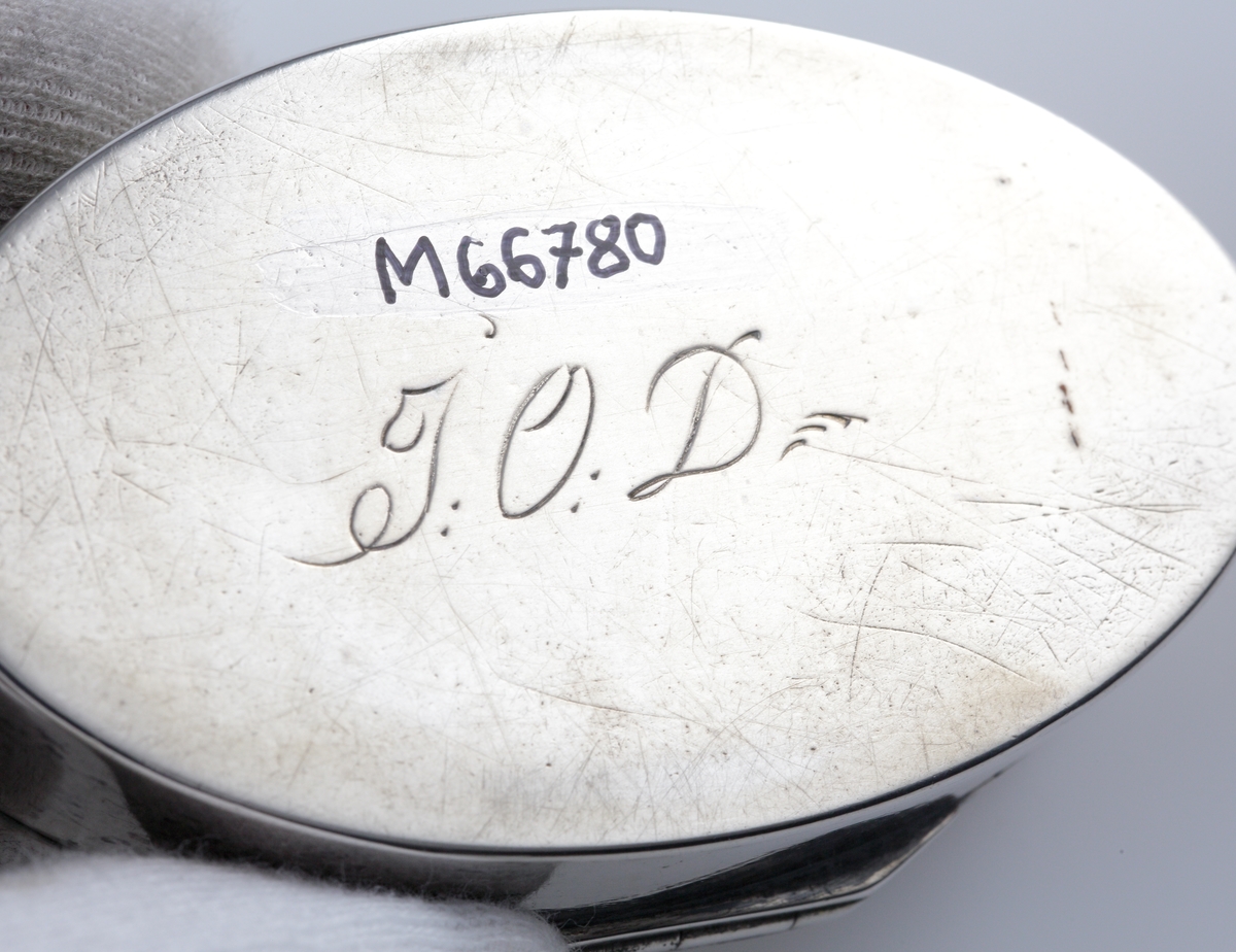 Dosa, silver.
Oval, slät modell. Invändigt förgylld. Ägarinitialer: "J.O.D." på dosans undersida. 
Stämplar (något otydliga) på lockets undersida.