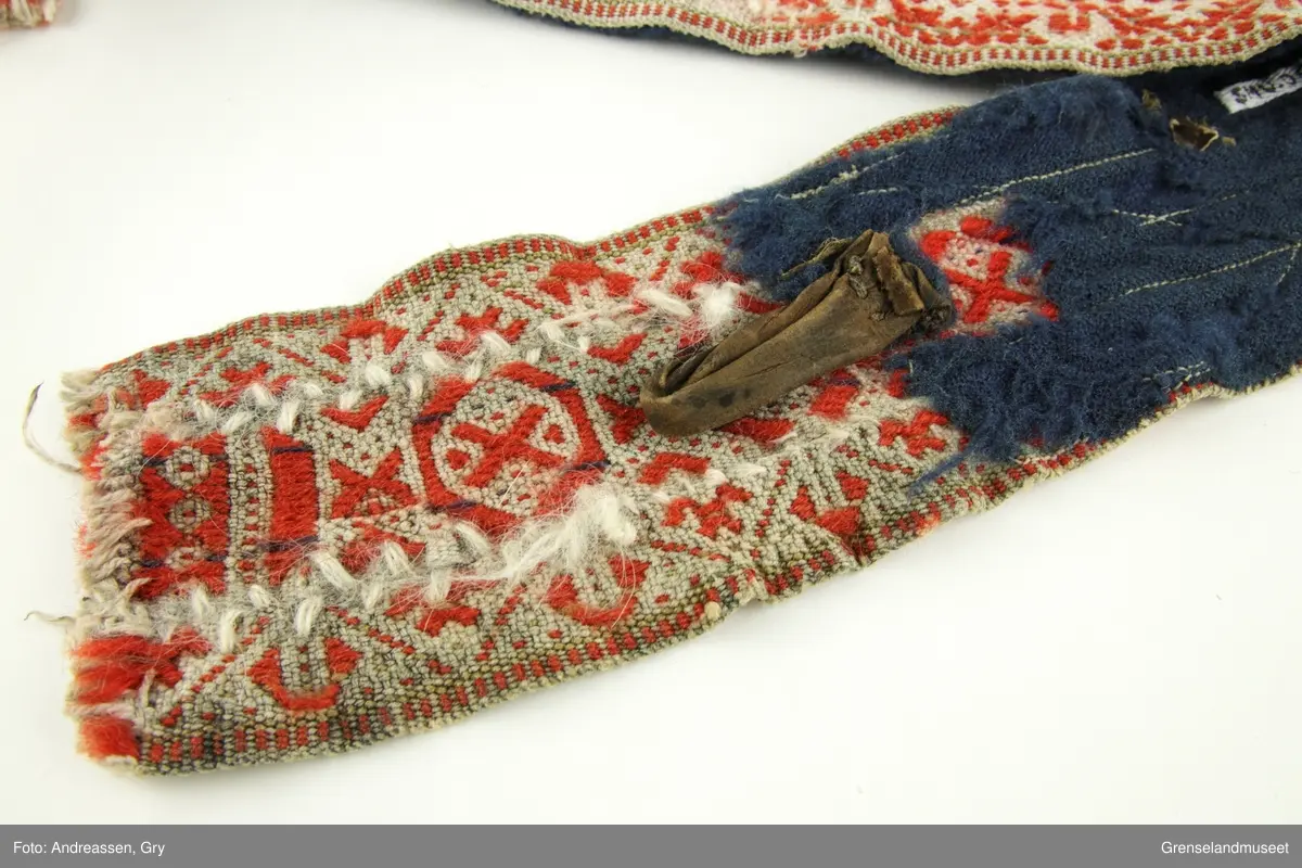 Vevd på grindvev i tre deler som er sydd sammen på langs. Sidestykkene har likt mønster. Bunn i hvitt bomullsgarn, dekor i rødt og litt blått plukk. Renningsrips. Lukning består av skinnhempe i den ene enden og skinnsnor i den andre enden. Beltet er foret med blått ullstoff.