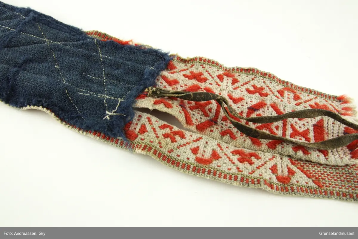 Vevd på grindvev i tre deler som er sydd sammen på langs. Sidestykkene har likt mønster. Bunn i hvitt bomullsgarn, dekor i rødt og litt blått plukk. Renningsrips. Lukning består av skinnhempe i den ene enden og skinnsnor i den andre enden. Beltet er foret med blått ullstoff.